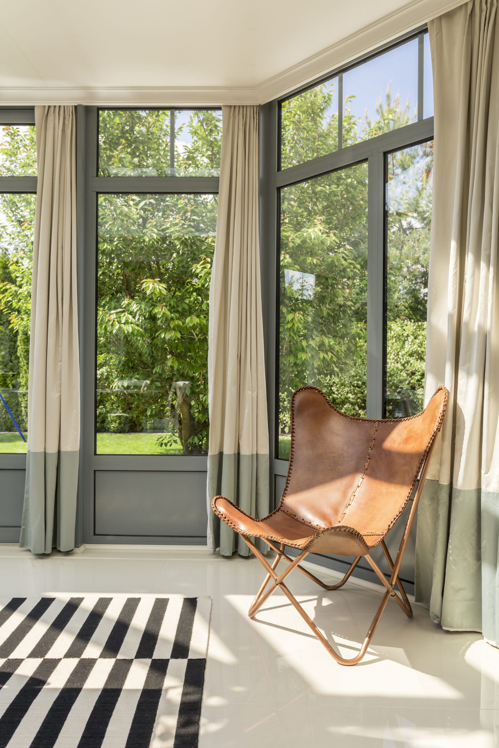 Minimalistic, leather armchair standing in room area, surrounded by windows, with stripy carpet on the floor