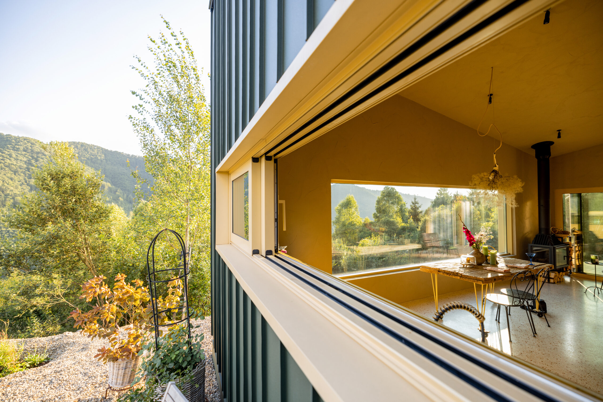 Perspective shot of an open slider windows summerville sc in a modern house, showcasing an elegant, nature-inspired interior. The lush greenery outside contrasts beautifully with the minimalist and cozy decor inside